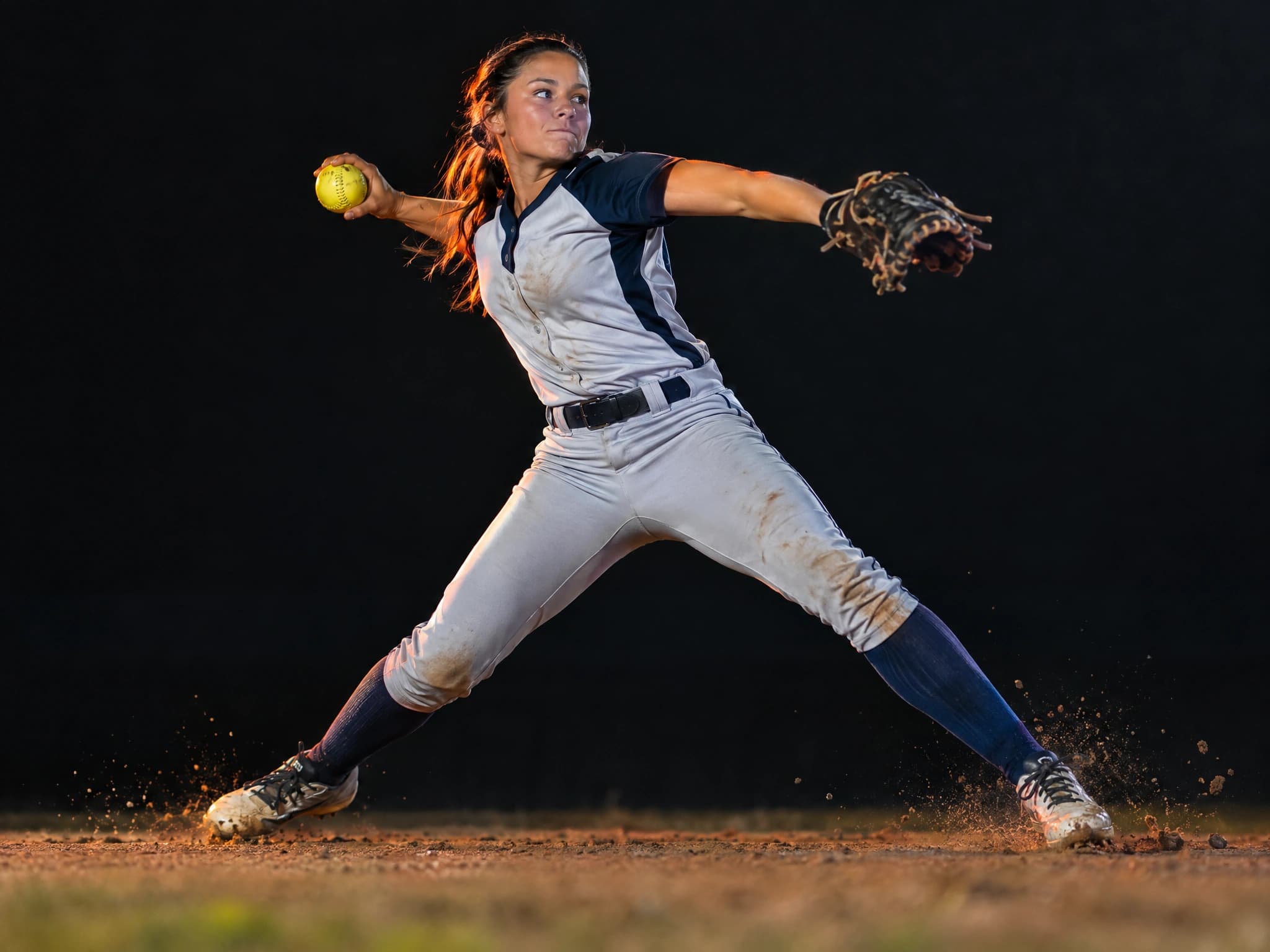 Softball player in uniform pants throwing across the diamond